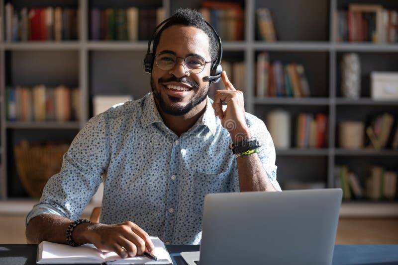 Happy young friendly african american man in eyeglasses wearing headset with mic, looking at camera. Smiling professional financial advisor consulting clients online, solving problems issues. Happy young friendly african american man in eyeglasses wearing headset with mic, looking at camera. Smiling professional financial advisor consulting clients online, solving problems issues.