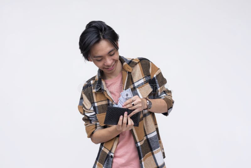 A happy young asian man taking out 100 dollar bills from his wallet. Isolated on a white background stock image