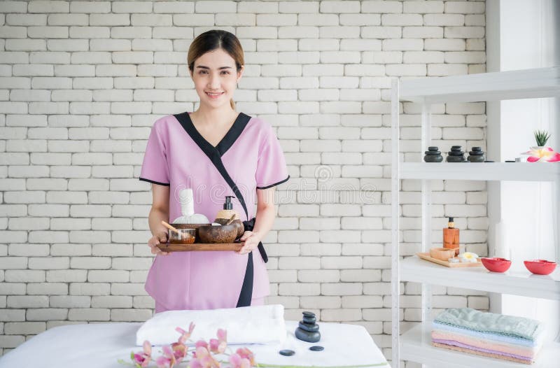 Happy young asian woman in uniform standing and holding tray of spa treatment accessories