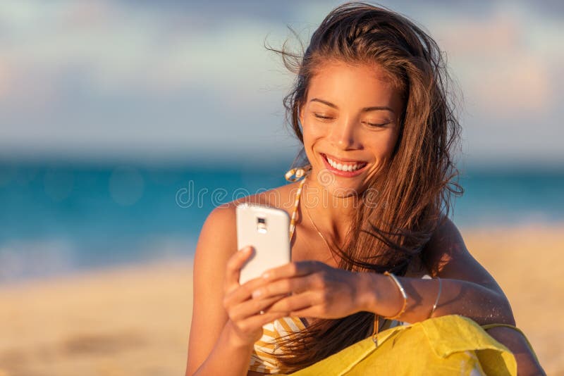 Happy young Asian woman using mobile phone texting online on beach vacation holiday travel summer lifestyle, Smiling