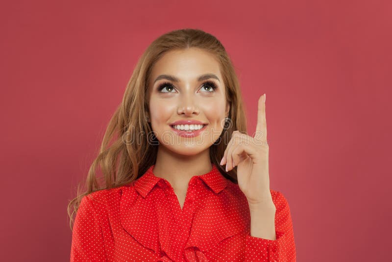 Happy young beautiful cheerful woman pointing up on colorful pink background portrait. Student girl pointing finger and looking up