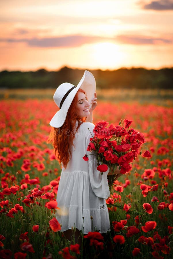 Happy Young beautiful female with bouquet of red poppies stands in flowered field at sunset stock image Happy Young beautiful female with bouquet of red poppies stands in flowered field at sunset stock image