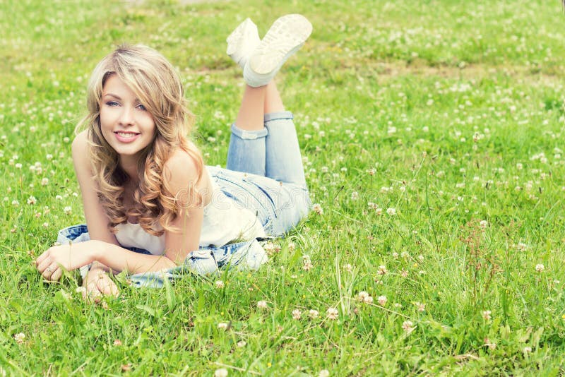 Happy young beautiful girl lying on the grass and smiles in jeans in a Sunny summer day in the garden