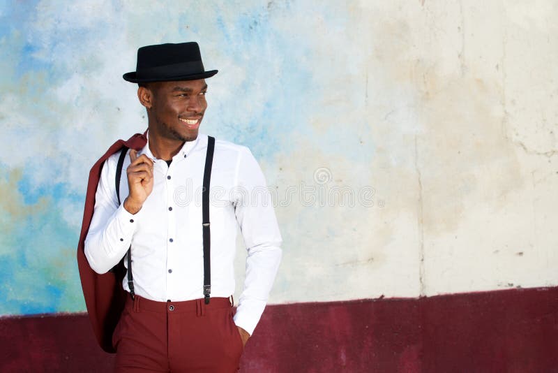 Happy Young Black Man with Suspenders and Hat Smiling by Wall Stock ...