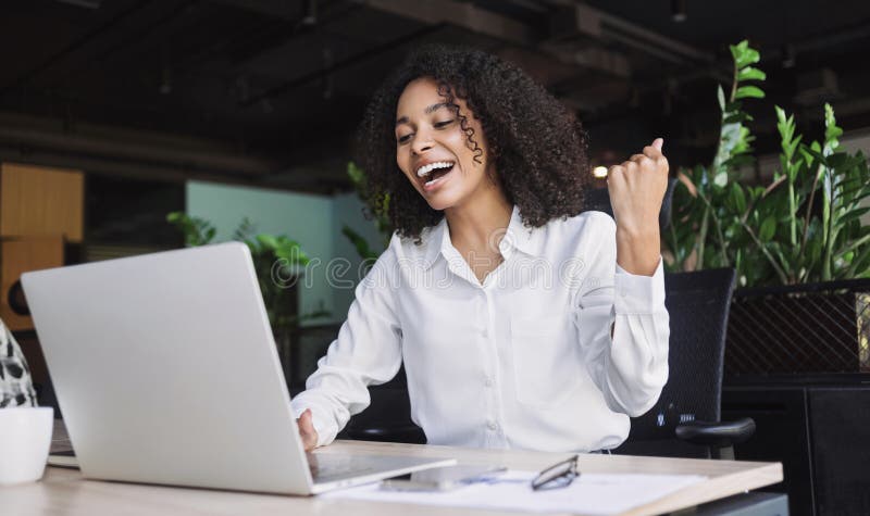 Happy young businesswoman looking at laptop computer in office, Excited african american woman working at her workplace