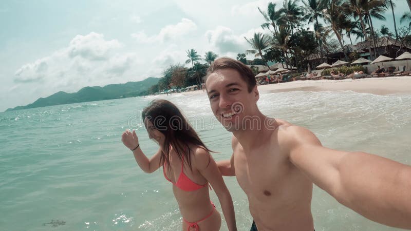 Happy young couple enjoying their vacation splashing in ocean on paradise tropical island. Turquoise water of ocean