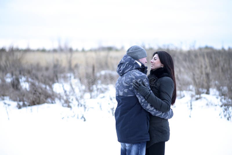 Happy young couple hugging outdoors in a snowy park. Love hugs, family relationships