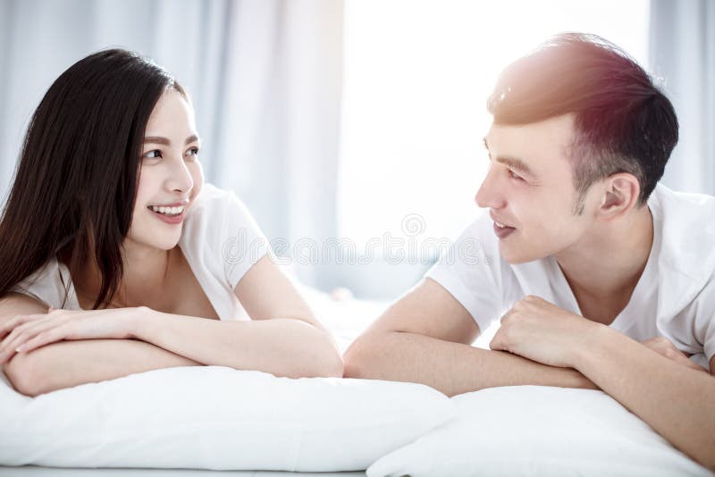 Happy young couple looking at each other and smiling while lying on bed stock photography Happy young couple looking at each other and smiling while lying on bed stock photography