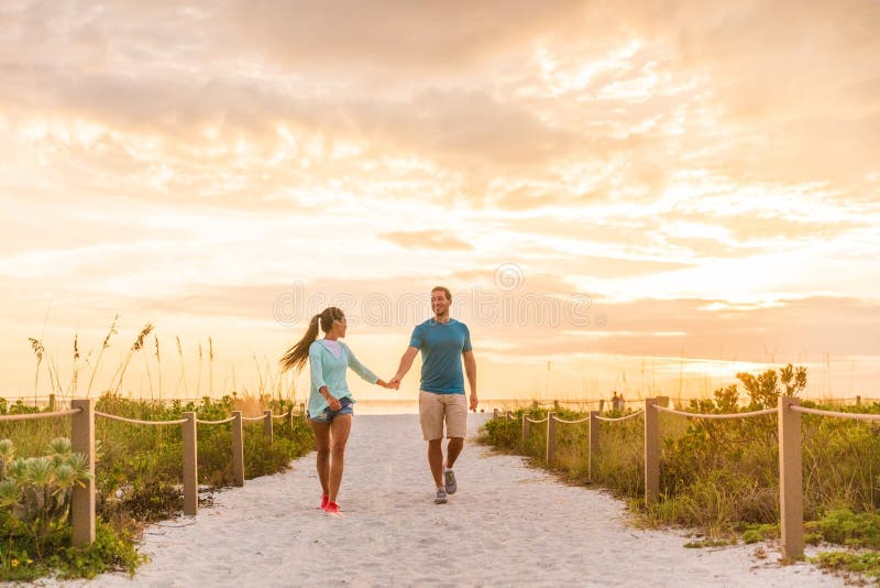 Happy young couple in love walking on romantic beach stroll at sunset. Lovers holding hands on Florida vacation holidays