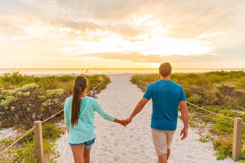 Happy young couple in love walking on romantic evening beach stroll at sunset. Lovers holding hands on summer holidays