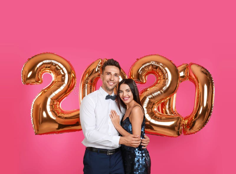 Happy young couple near golden 2020 balloons on pink background stock photography Happy young couple near golden 2020 balloons on pink background stock photography