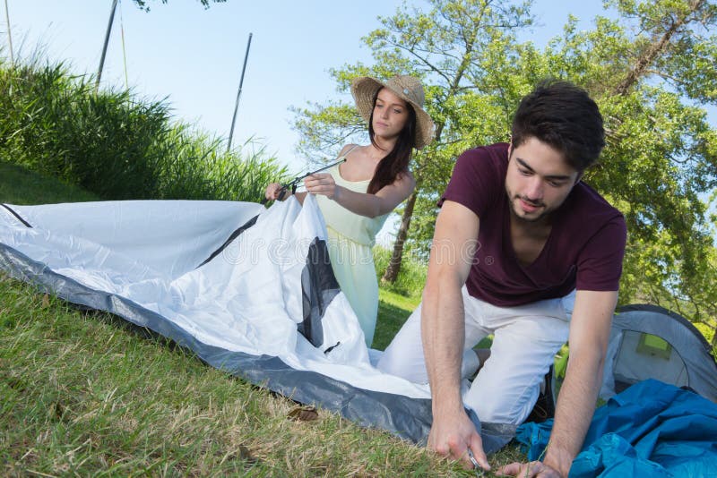 Happy young couple setting up their tent at camping site stock images Happy young couple setting up their tent at camping site stock images