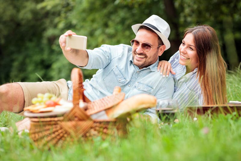 Happy young couple taking a selfie while enjoying picnic time in park royalty free stock photography Happy young couple taking a selfie while enjoying picnic time in park royalty free stock photography