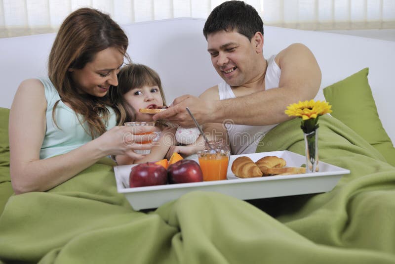 Happy young family eat breakfast in bed