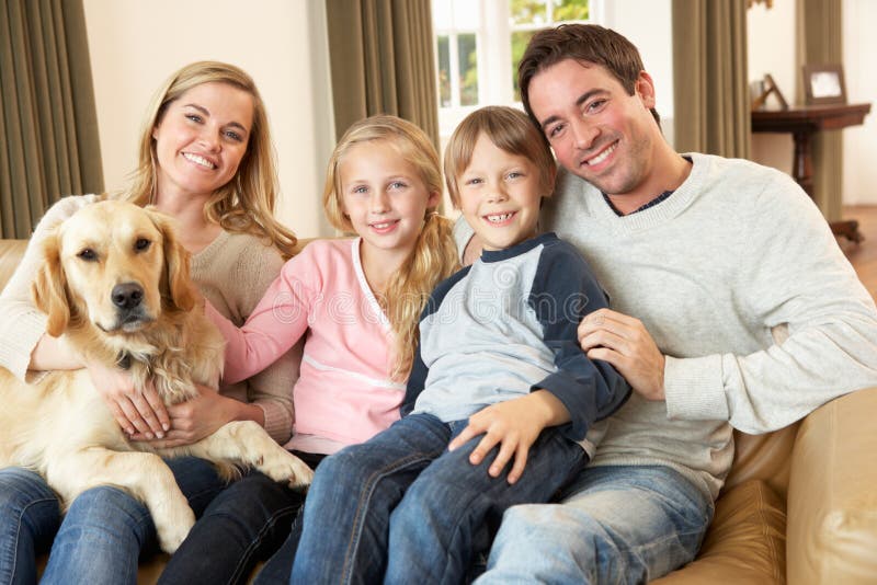 Glückliche junge Familie sitzt auf dem sofa hält einen Hund Lächelnd.