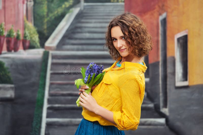 Happy young fashion woman with bouquet of flowers walking on city street Stylish female model wearing yellow shirt and blue skirt. Happy young fashion woman with bouquet of flowers walking on city street Stylish female model wearing yellow shirt and blue skirt