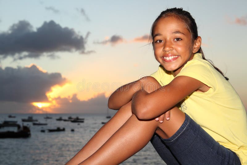 Happy young girl sitting by seaside at sunset