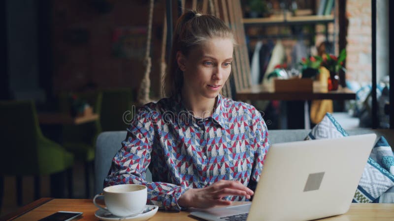 Happy young lady working with laptop in cafe typing sitting at table alone stock video footage