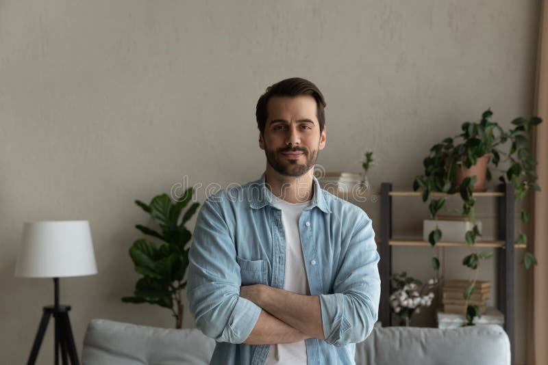 Looking ahead with confidence. Portrait of happy young male buyer of house flat standing at home in living room with arms crossed. Successful man owner of new apartment look at camera enjoy wellbeing. Looking ahead with confidence. Portrait of happy young male buyer of house flat standing at home in living room with arms crossed. Successful man owner of new apartment look at camera enjoy wellbeing