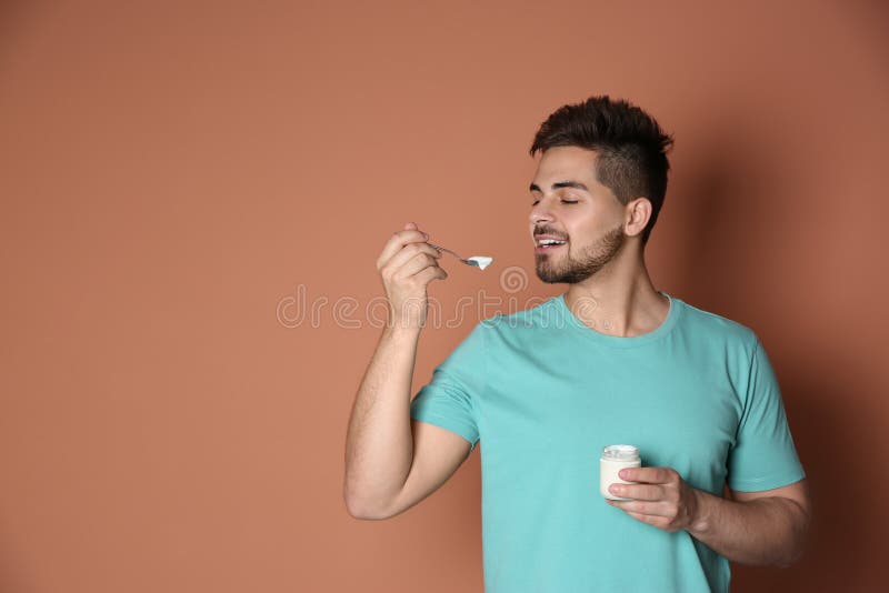 Happy Young Man Eating Tasty Yogurt on Background. Space for Text Stock