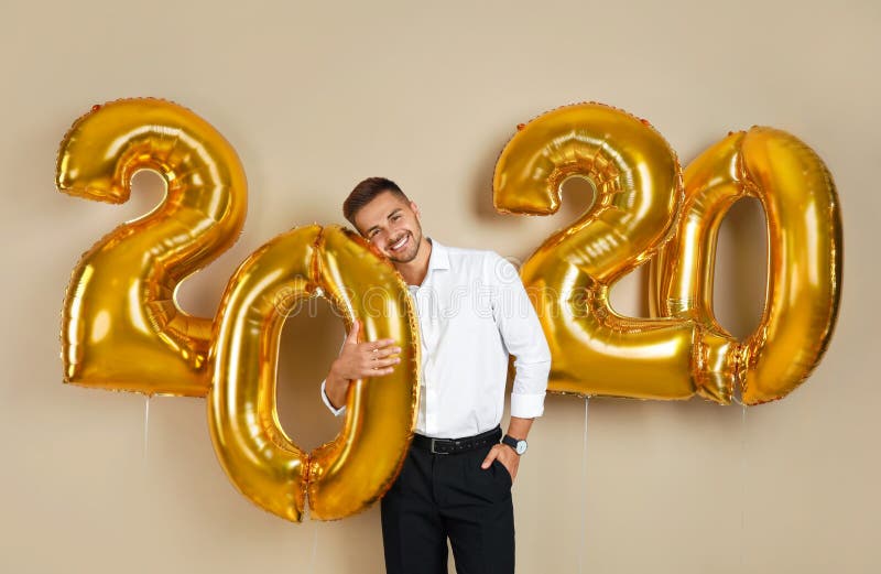 Happy young man with golden 2020 balloons on beige royalty free stock images Happy young man with golden 2020 balloons on beige royalty free stock images