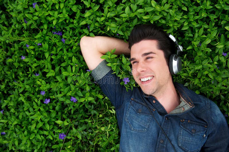 Happy young man lying on grass, listening to music