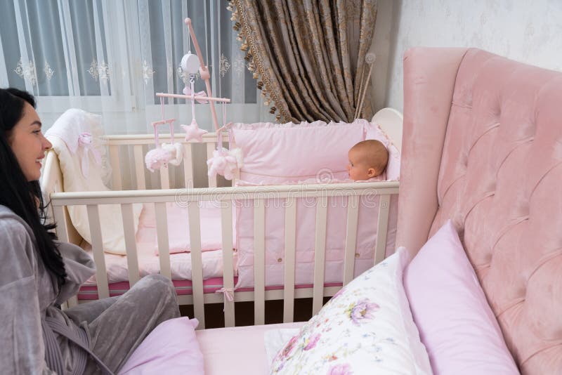 Happy young mother and baby in pink bedroom scene.