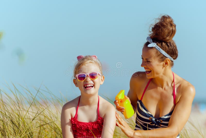 Happy young mother and child on ocean coast applying SPF