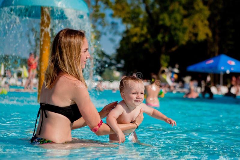 Happy young mother and her little son, adorable laughing baby boy having fun together in an outdoor swimming pool on a hot summer