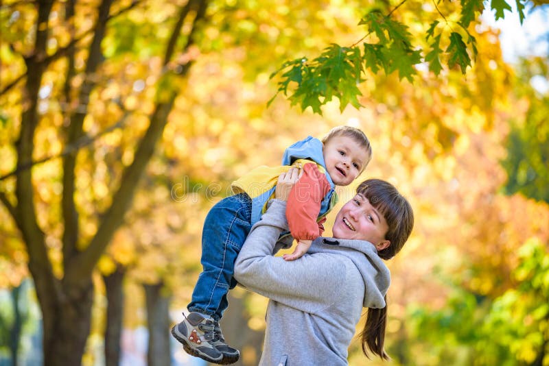 Happy young mother holding sweet toddler boy, family having fun together outside on a nice sunny autumn day. Cute adorable kid and royalty free stock photography Happy young mother holding sweet toddler boy, family having fun together outside on a nice sunny autumn day. Cute adorable kid and royalty free stock photography