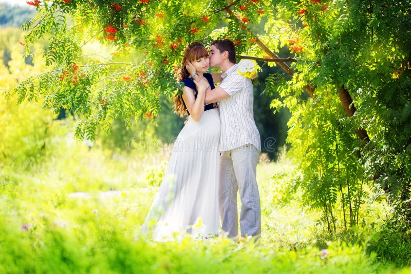 Happy and young pregnant couple hugging in the park. Summer vacation. New life concept. Future mother and father. stock image Happy and young pregnant couple hugging in the park. Summer vacation. New life concept. Future mother and father. stock image