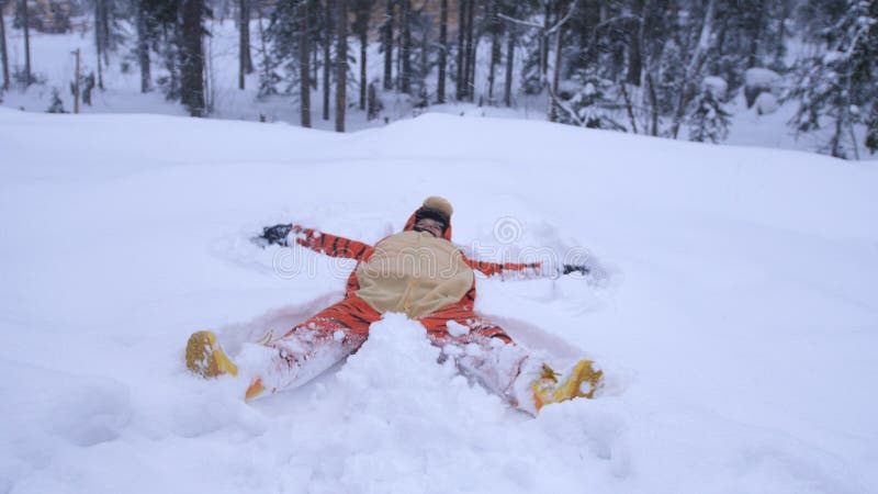 Happy young pretty woman wearing funny tiger suit lying in snowdrift in winter forest