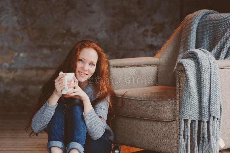 Happy young readhead woman drinking hot coffee or tea at home. Calm and cozy weekend in winter stock photo Happy young readhead woman drinking hot coffee or tea at home. Calm and cozy weekend in winter stock photo