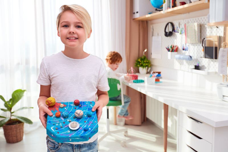 Happy young school kid, boy showing the model of solar system made from plasticine, kids room background