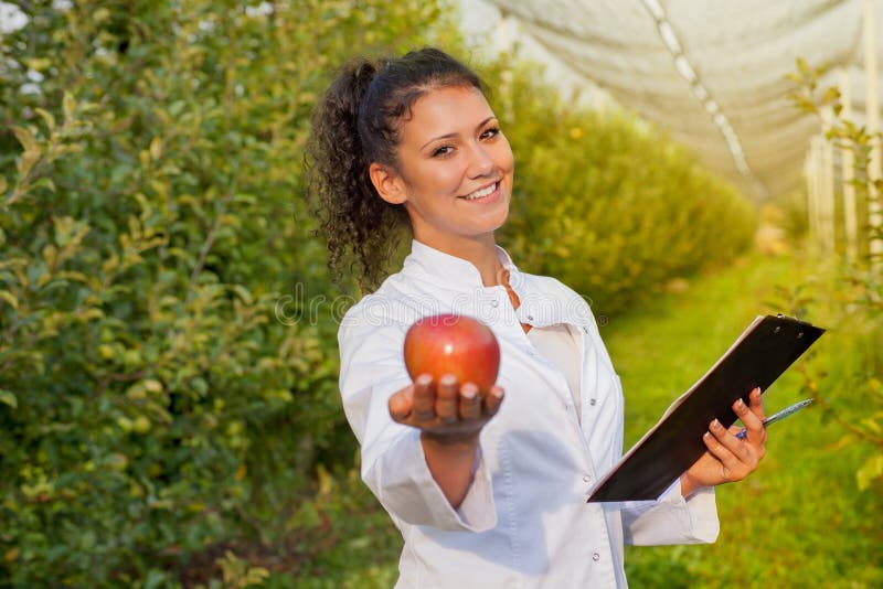 Happy young woman agronomist with red organic apple in her hand