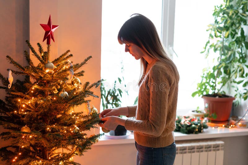 Happy young woman decorating christmas tree at home. Winter holidays in a house interior. Golden and white Christmas royalty free stock photos Happy young woman decorating christmas tree at home. Winter holidays in a house interior. Golden and white Christmas royalty free stock photos