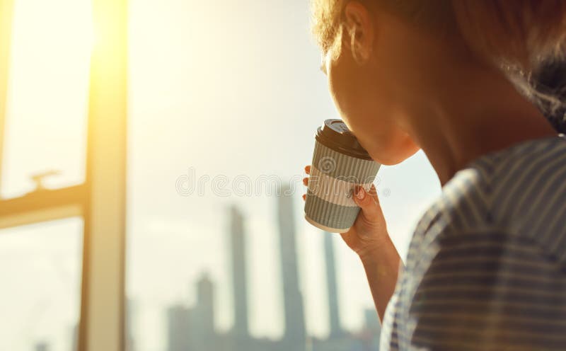 Happy young woman drinks coffee in morning at window