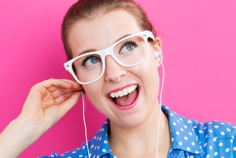 Happy young woman with earbuds on pink background