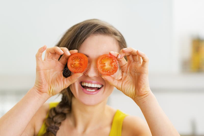 Happy young woman holding two slices of tomato in front of eyes