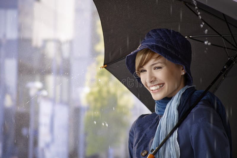 Happy young woman holding umbrella in rain