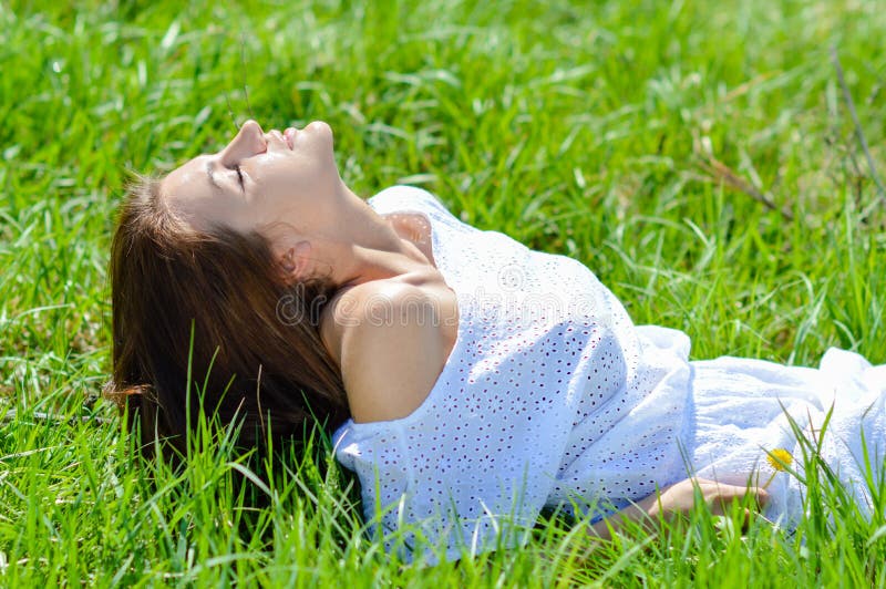 Happy young woman lying in short white summer dress on green grass