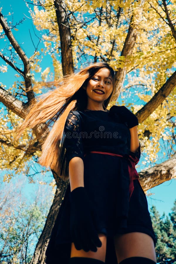 Happy young woman in park on sunny autumn day, smiling. Cheerful beautiful girl in black retro dress autumn fashion style