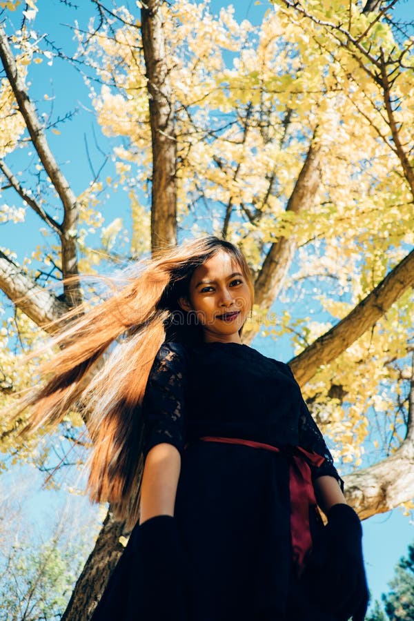 Happy young woman in park on sunny autumn day, smiling. Cheerful beautiful girl in black retro dress autumn fashion style