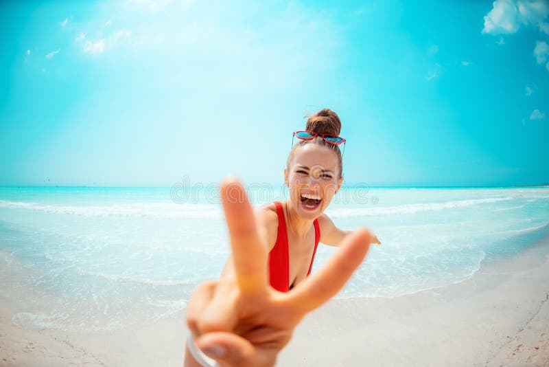 Happy young woman in red swimsuit on seacoast showing victory