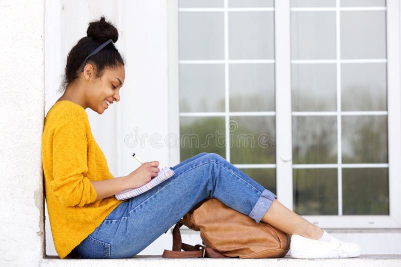 Side view portrait of happy young woman sitting outdoors writing a book