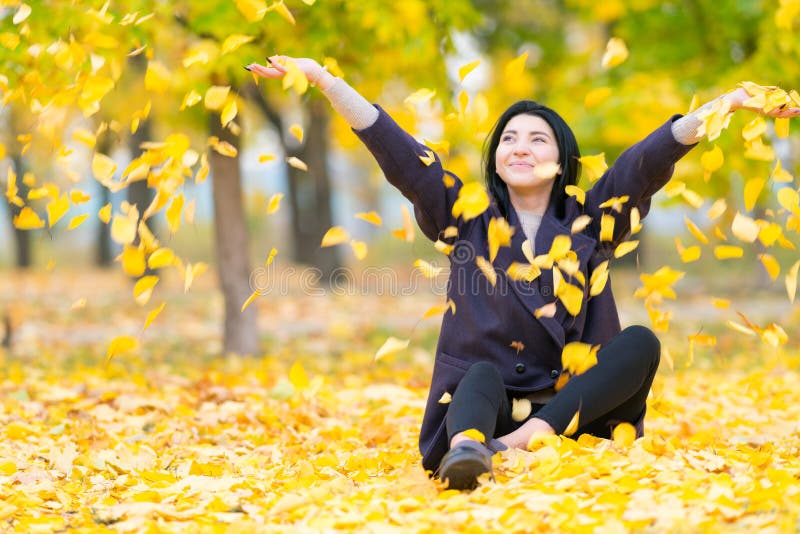 Happy young woman throwing yellow autumn leaves.