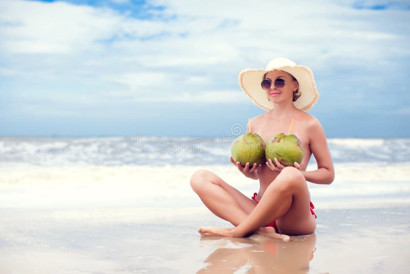 Happy young woman topless with coconuts in straw hat with on the beach with a coconut