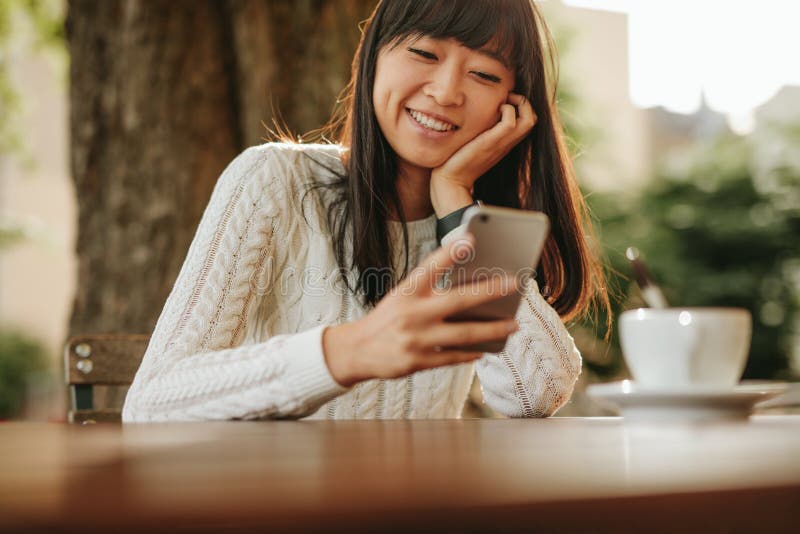 Happy young woman using her cellphone at cafe