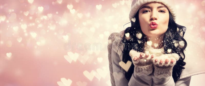 Happy young woman with winter clothes blowing snow and hearts. Happy young woman with winter clothes blowing snow and hearts