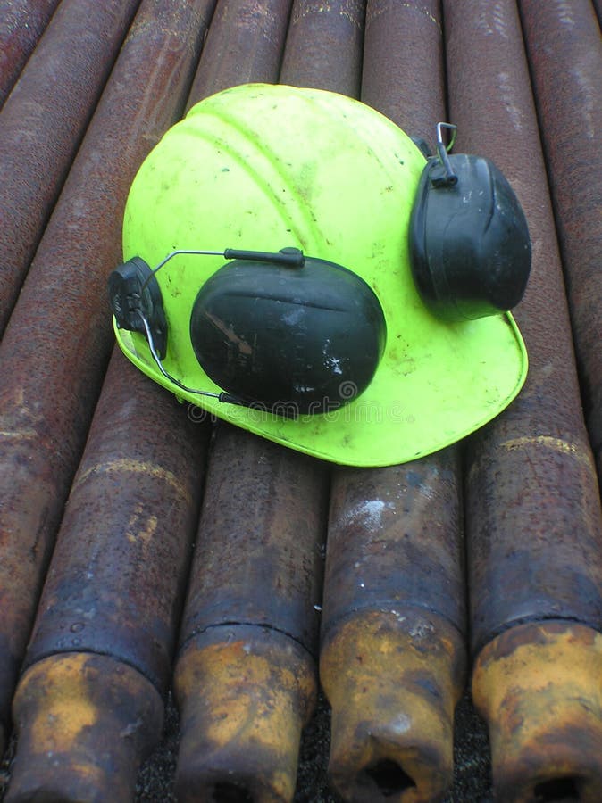 Hard hat and ear muffs on drilling rig pipes